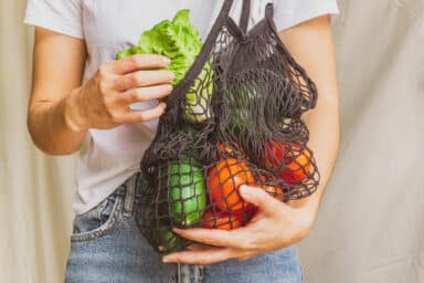 Woman holding mesh shopping bag full of produce.